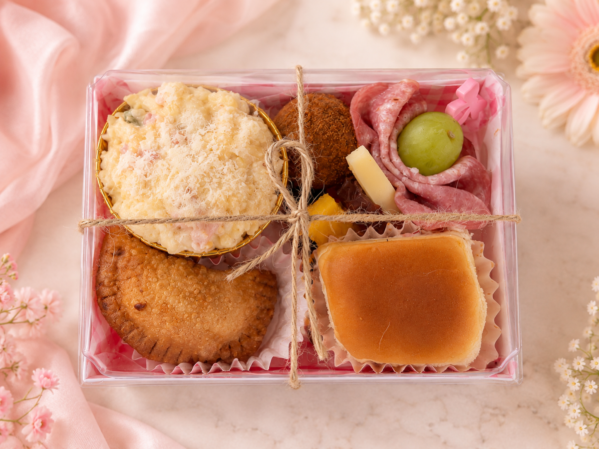 Pink first-birthday Añejo Cajita with a Hawaiian roll, empanada, croqueta, creamy party salad, and grazing bite